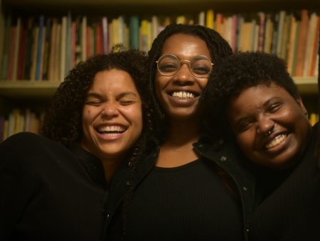 Nessa, Mali, and Kah laugh together in front of a bookcase